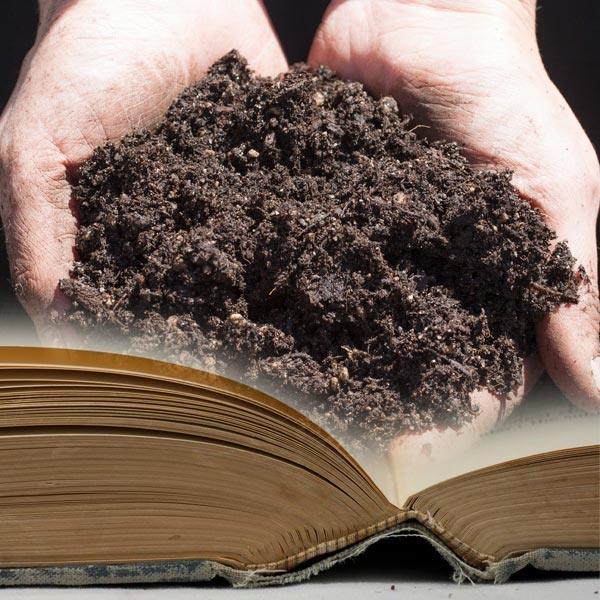 Hands holding dark compost above an open book
