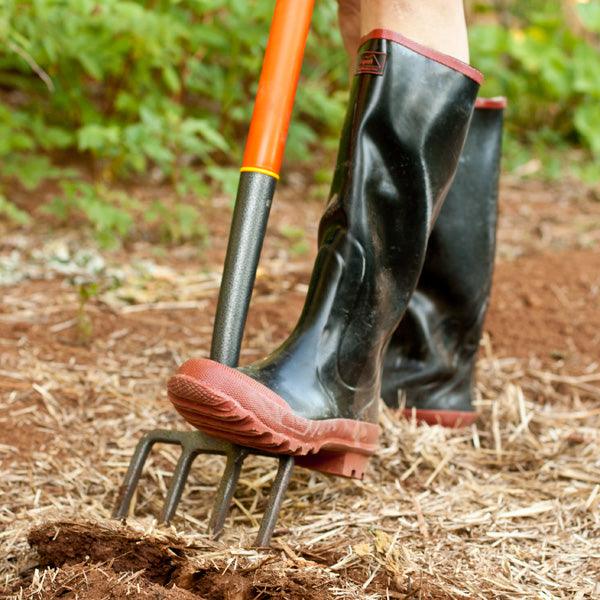 Boot pressing a garden fork into soil