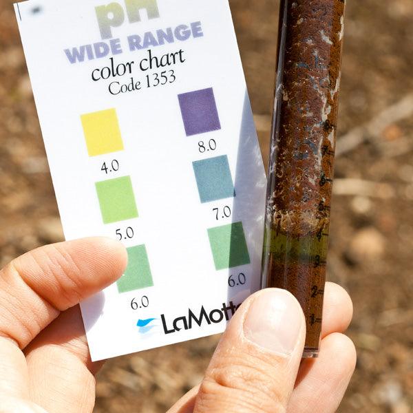 Hand comparing a soil sample to a pH color chart