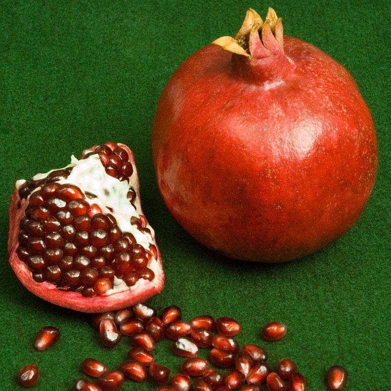 Whole red pomegranate and cut wedge with arils on green